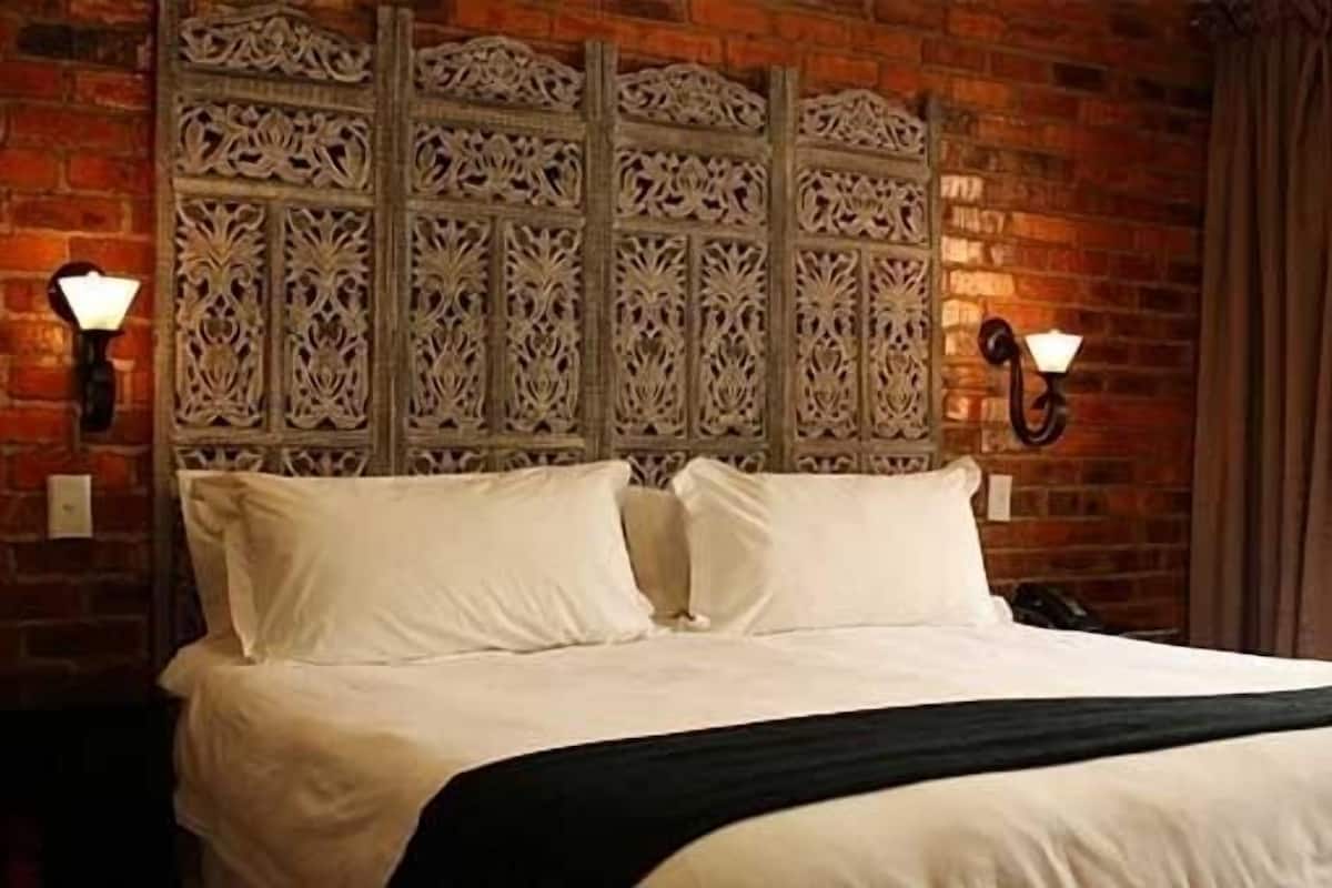 Un lit avec du linge de lit blanc, un jeté noir et une tête de lit décorative ornée de motifs complexes.