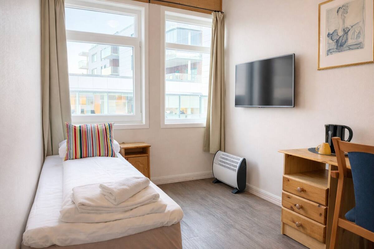 A hotel room with a bed, a desk, a chair, a TV, and a radiator.