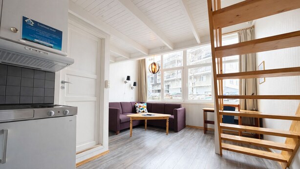 Eine moderne Küche mit Einbauherd, einem violetten Sofa, einem Holztisch und Blick auf die Stadt durch große Fenster.