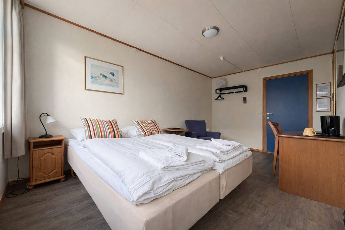 A hotel room with a bed, a desk, a chair, a lamp, and a painting on the wall.
