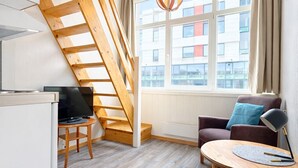 Ein modernes Interieur mit schrägverdeckter Decke, einer Holztreppe, einem Sofa, einem Tisch und einem Fernseher.