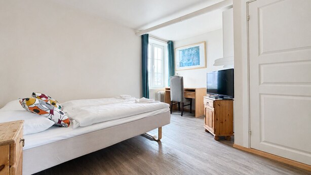 A bedroom with a bed, a desk, a chair, a television, and a wardrobe.