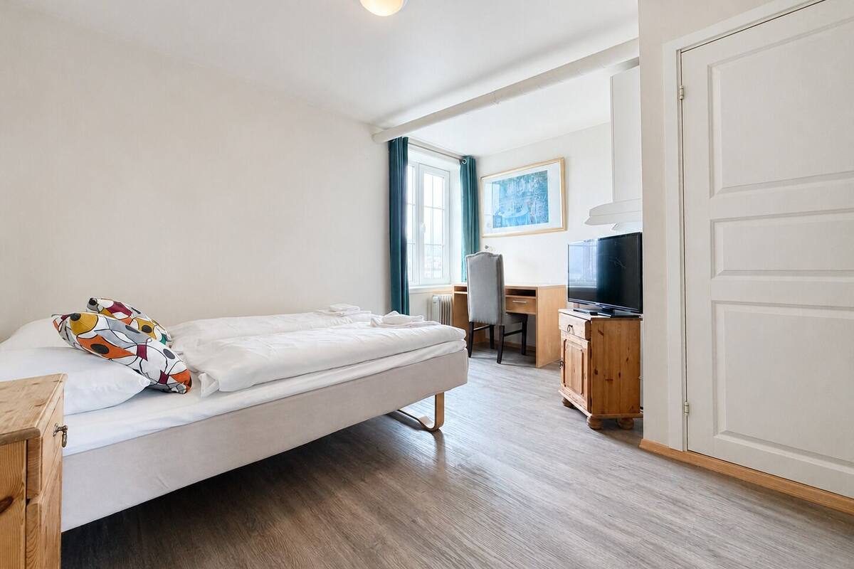 A bedroom with a bed, a desk, a chair, a television, and a wardrobe.