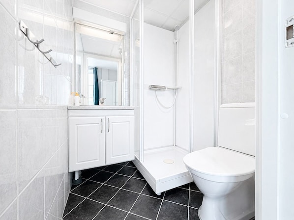 A modern bathroom with a white toilet, a shower enclosure, and a vanity with cabinets. - Hotel Toranes (Mo-I-Rana)