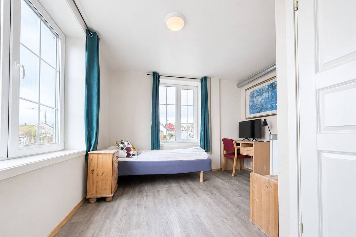 A compact room with a bed, a desk, a chair, and a window with curtains.