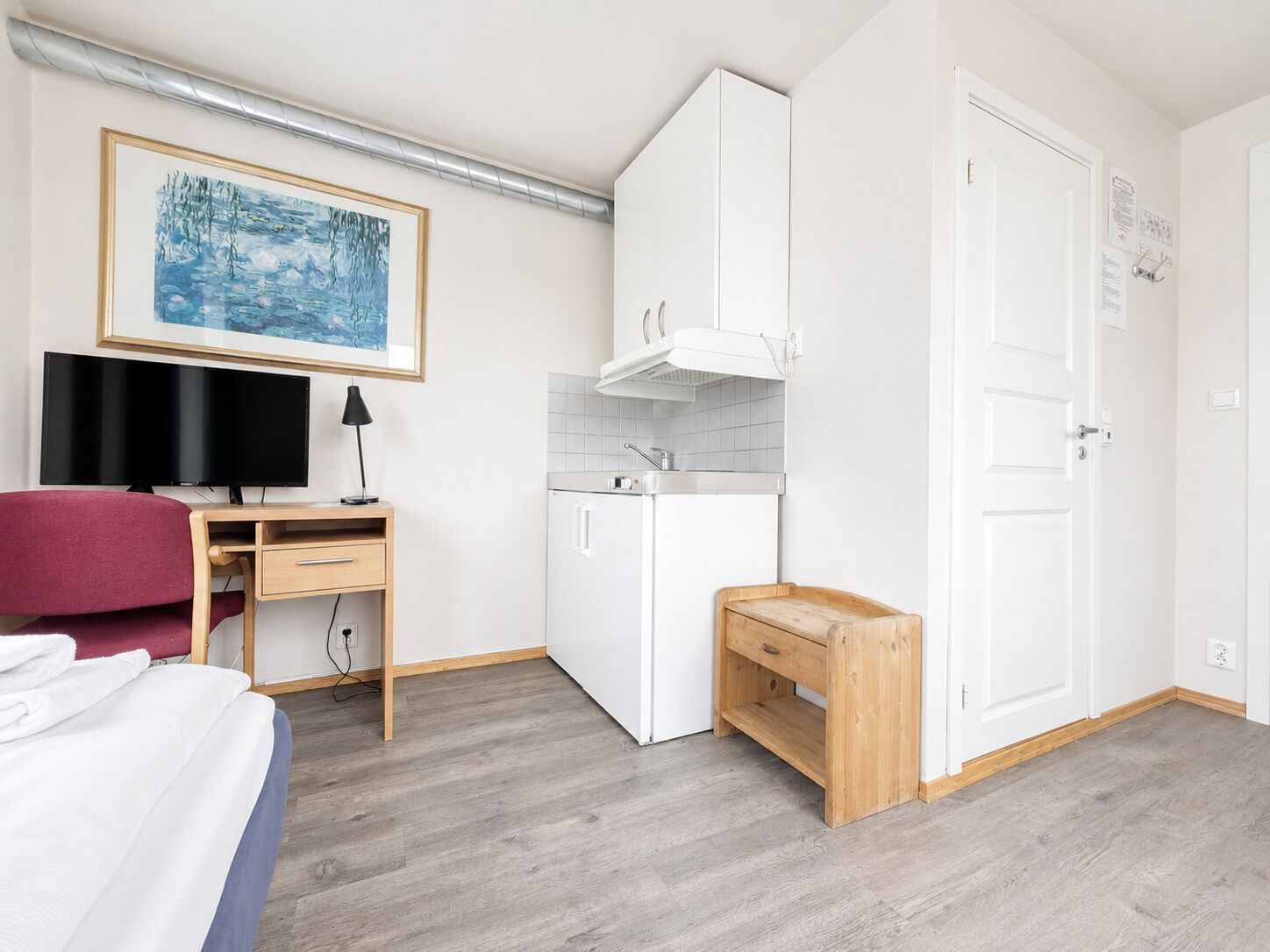 Een compacte kamer met een bed, een bureau met computer, een kleine kitchenette en een kledingkast.