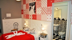 A bedroom with a red bedspread, a white headboard, and a wall decorated with various patterns. There is a poster with the word "GHOST" and a mirror above the bed. - I Love Piramide (Rome)