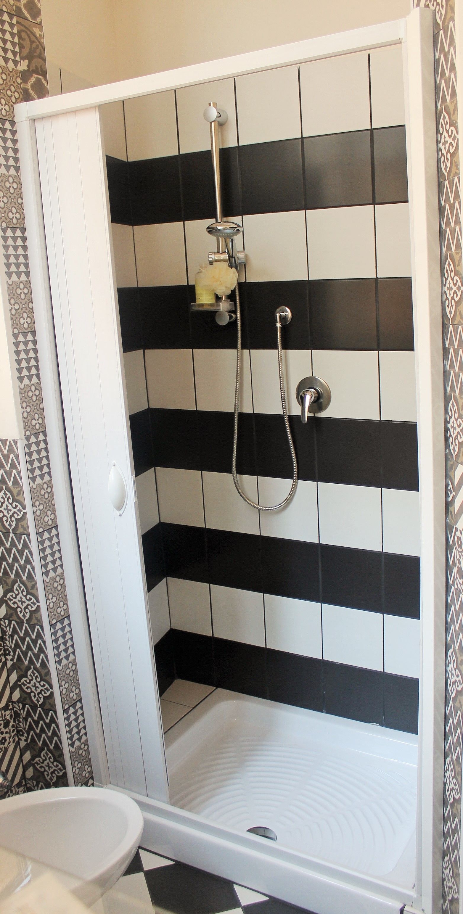 Zona de ducha con baldosas blanco y negro, una puerta blanca y un lavamanos blanco.