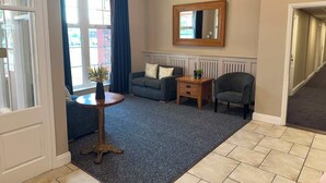 A living room with a sofa, a side table, a chair, a mirror, and a view of the outside. - Northallerton Motel (Northallerton)