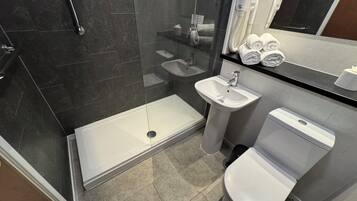 Un baño moderno con ducha envuelta en vidrio, lavamanos sobre pedestal, inodoro y espejo sobre el lavamanos.
