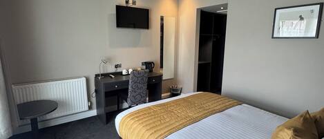 Una camera d'hotel con un letto, una scrivania, una sedia, un termosifone, una televisione e un quadro appeso al muro.