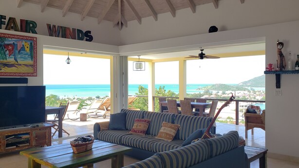 A living room with a large TV, a sofa, and a view of the ocean. - Villa Fair Winds (Jolly Harbour)