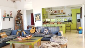A living room with a striped sofa, a colorful coffee table, and a guitar. - Villa Fair Winds (Jolly Harbour)