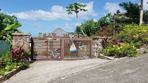 A gated entrance with a wooden gate, surrounded by lush greenery and tropical plants. - Villa Fair Winds (Jolly Harbour)