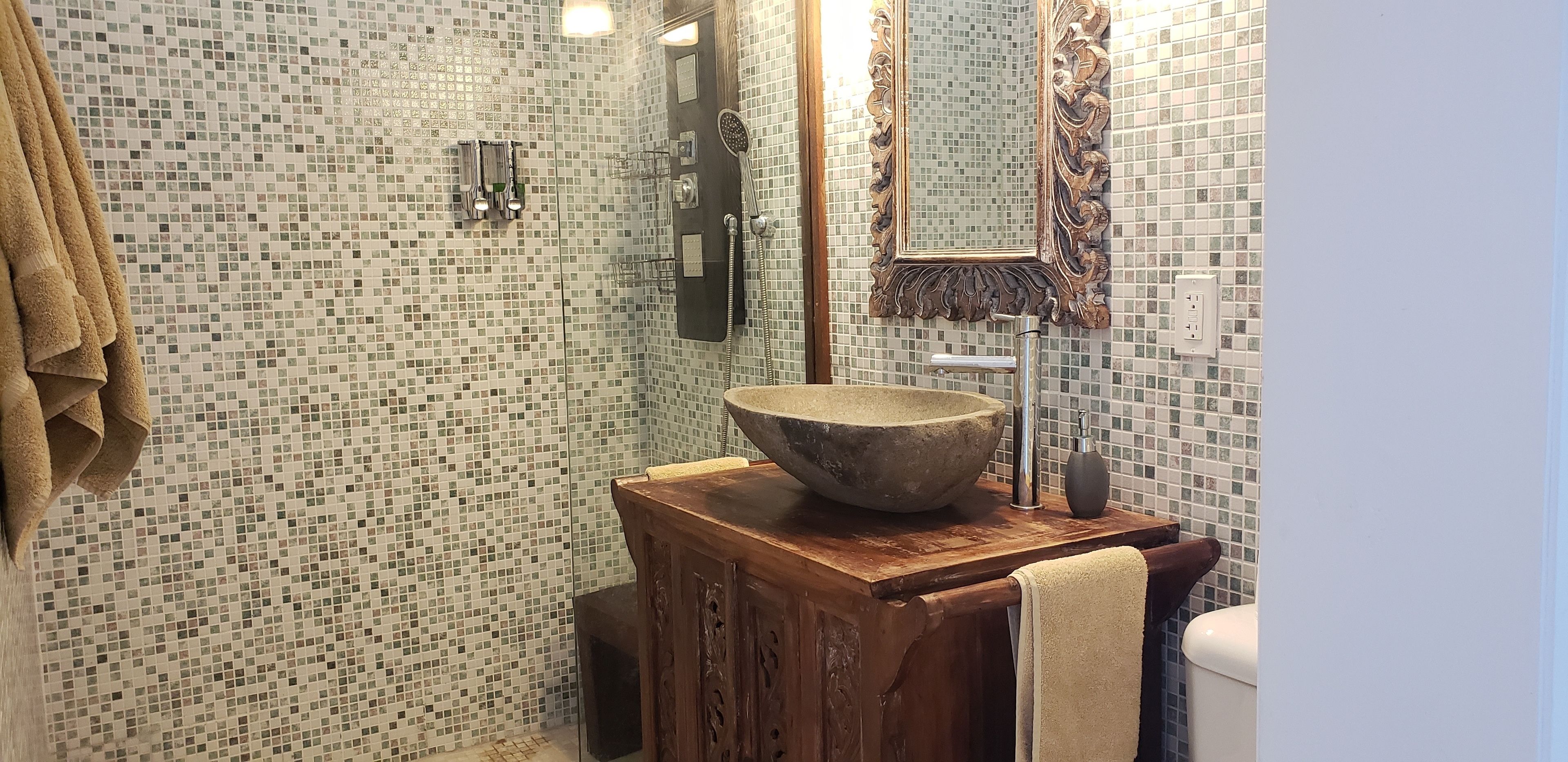 A bathroom with mosaic tile walls, a wooden vanity with a large bowl sink, a mirror with an ornate frame, and a towel rack with towels.