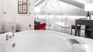 A modern bathroom with a large white bathtub, a red chair, and a framed artwork on the wall. - Hotel Villa Fanny (Cagliari)