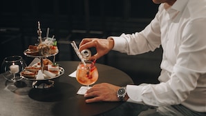 A person in a white shirt pouring a drink into a glass on a round table with a dessert tray and a candle. - Hotel Villa Fanny (Cagliari)
