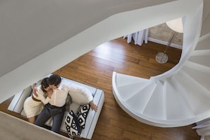 Un interno moderno con una scala a chiocciola, pavimento in legno e una zona salotto con cuscini decorati.