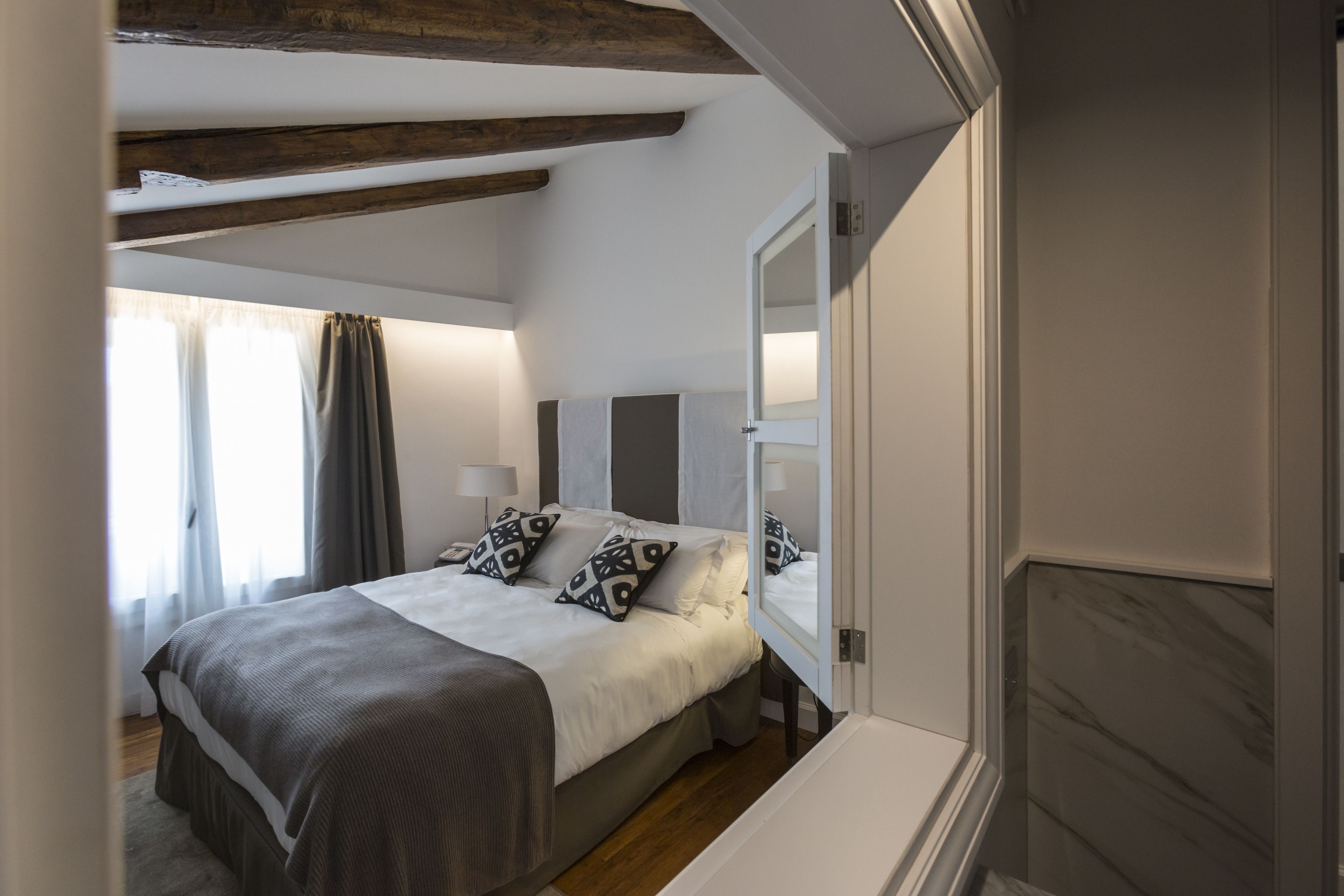 A bedroom with a bed, bedside tables, a mirror, and a window with curtains.