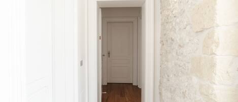 A hallway with a wooden floor, white walls, and a stone accent wall.