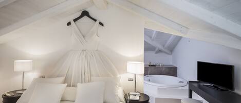 A bedroom with a large bed, bedside lamps, a TV, and a view of a bathroom with a bathtub and a shower.