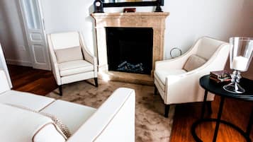 A living room with a fireplace, two white armchairs, a coffee table, and a side table with a candle.