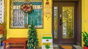 A yellow building with a decorative wreath on a window, a small Christmas tree, and a welcome sign. - Silver Netherlands B and B (Luodong)