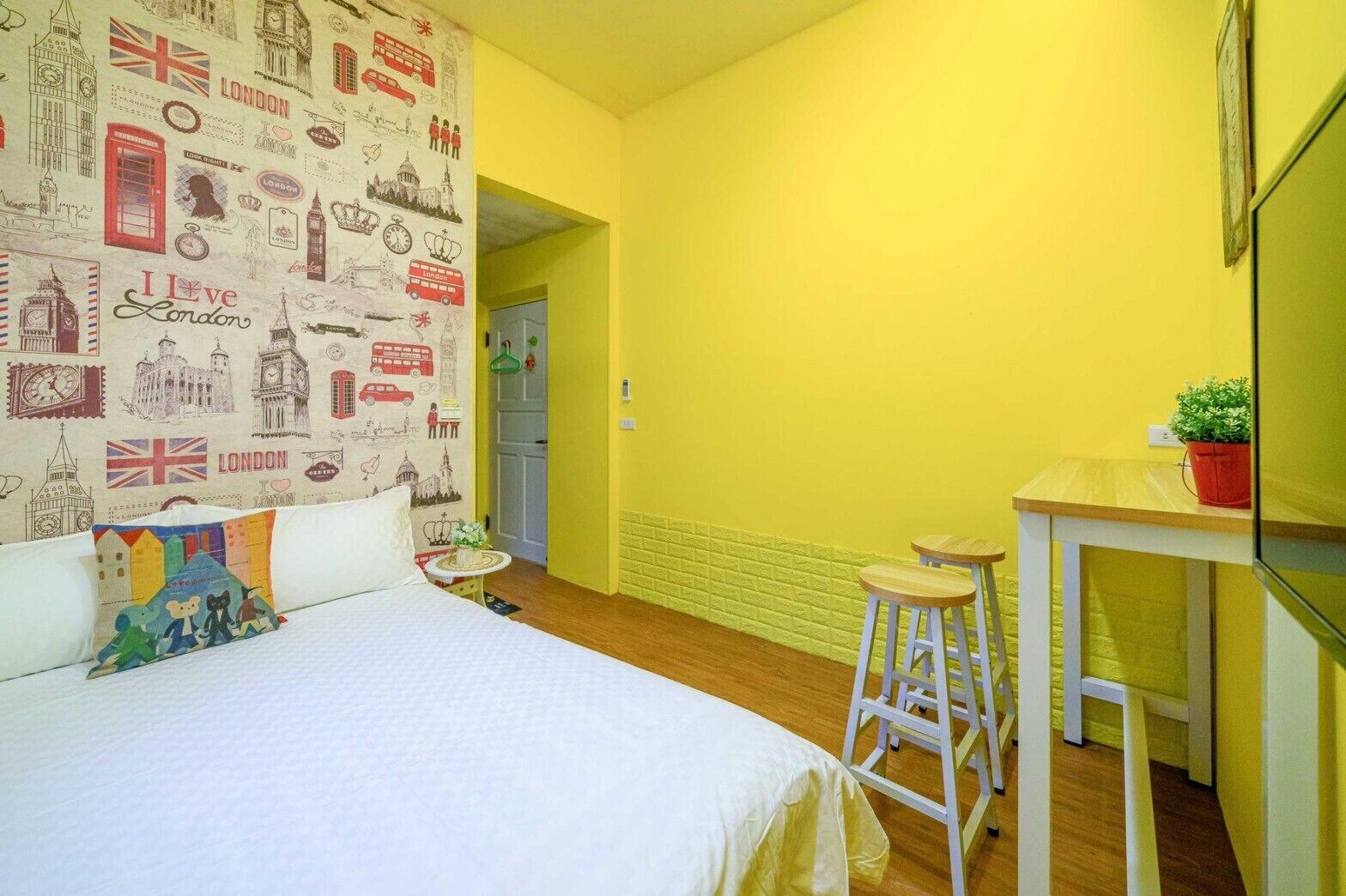 A room with a bed, a desk, and a stool. There is a wall with a pattern of London landmarks.