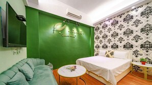 A room with a green accent wall, a bed with white bedding, a grey sofa, a round wooden table, and a patterned wallpaper. - Silver Netherlands B and B (Luodong)
