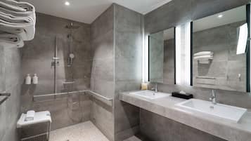 Un baño moderno con cabina de ducha, dos lavamanos, un espejo grande y toallas ordenadas.