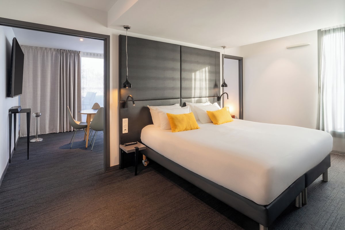 A hotel room with a large bed, bedside tables, a flat-screen TV, and a view of the city.