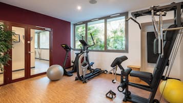 Un gimnasio en casa con equipo de ejercicio, un ventanal grande y suelo de madera.