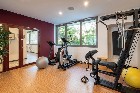 Une salle de sport à domicile équipée de matériel d’exercice, dotée d’une grande fenêtre et d’un plancher en bois.