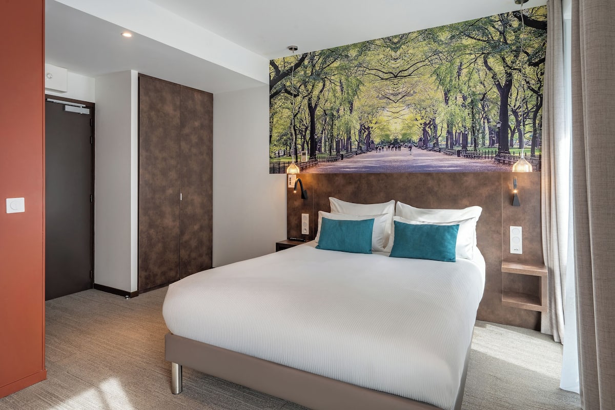 A hotel room with a large bed, a headboard with a park mural, bedside lamps, and a wardrobe.