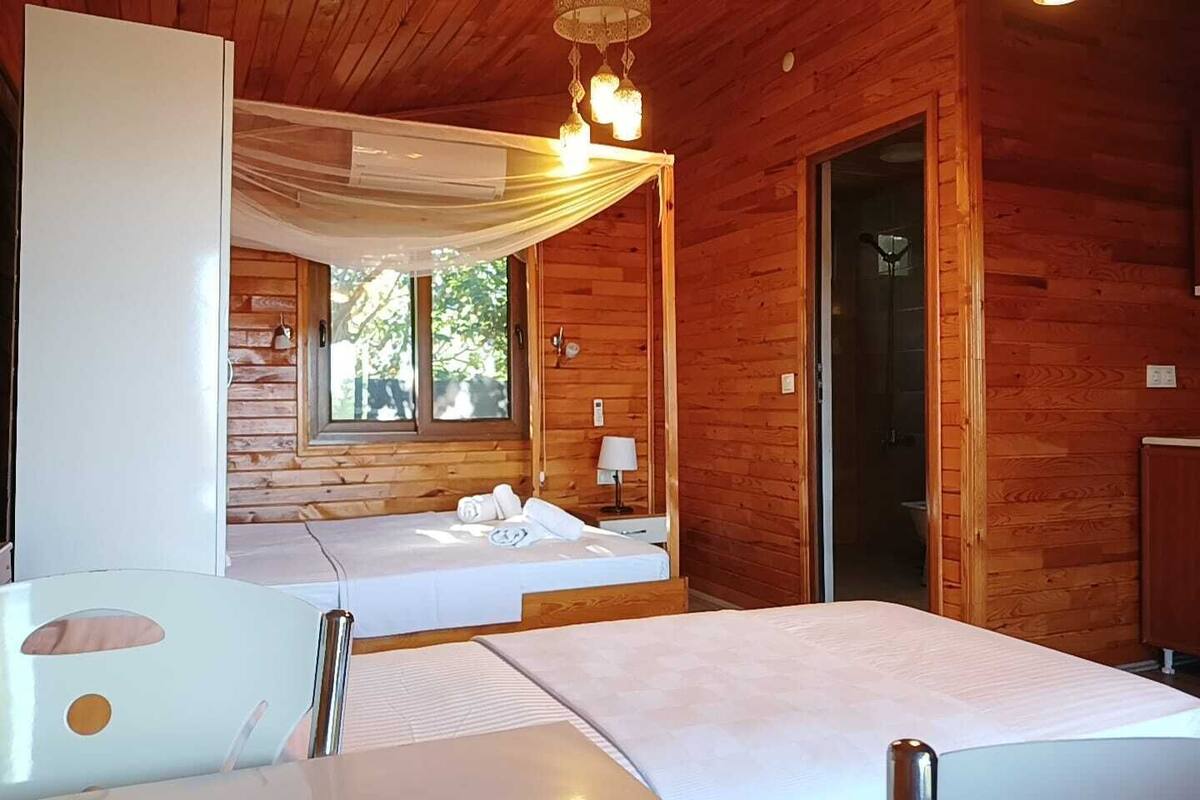 A wooden cabin room with two beds, a table, and a window.