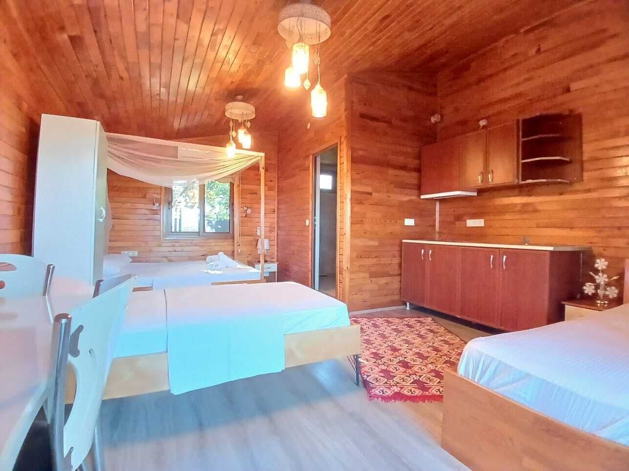 A wooden cabin with two beds, a wardrobe, and a small kitchen area.