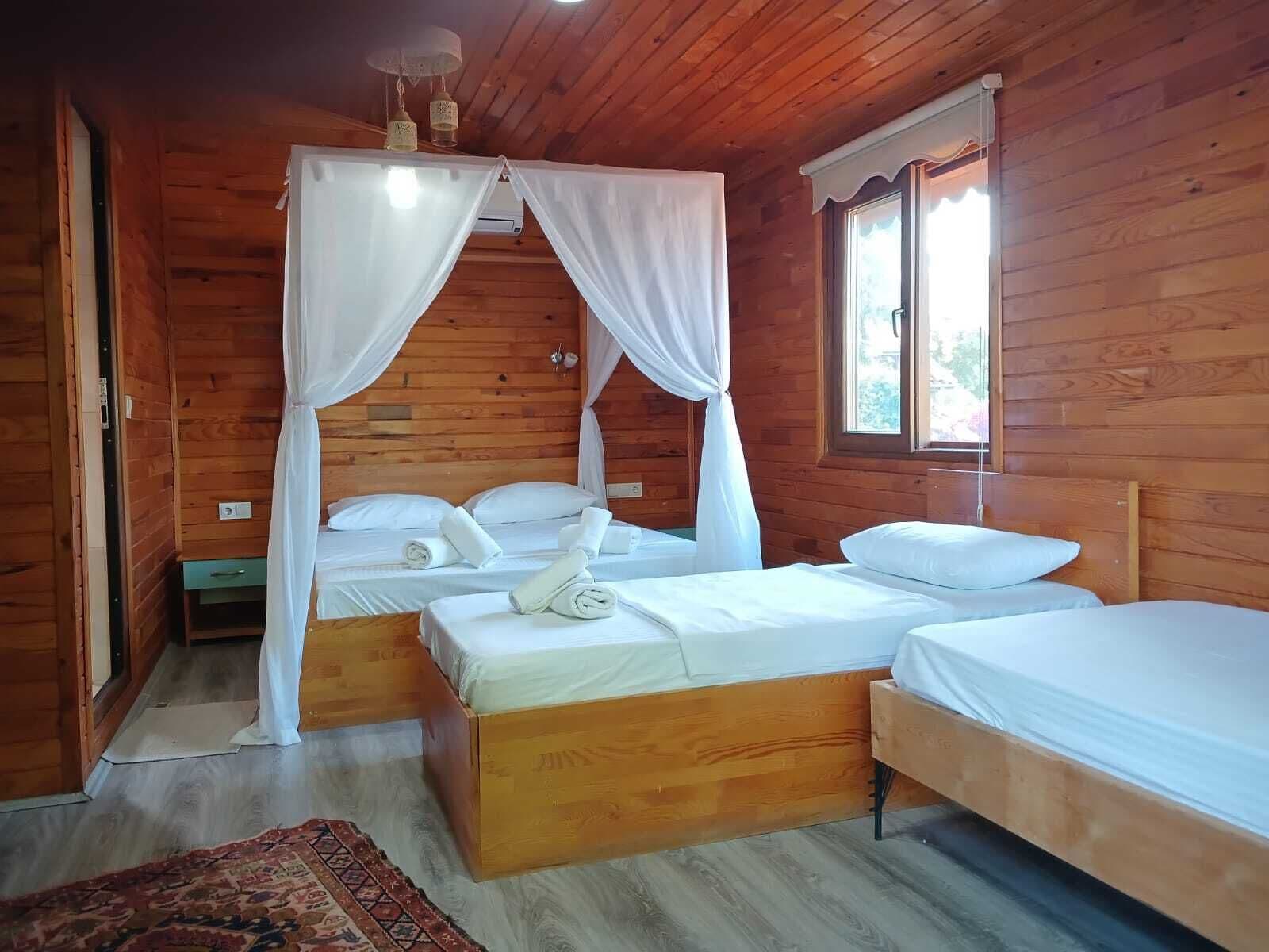 A wooden cabin room with two beds, one with a canopy and white bedding, and a window with a view.