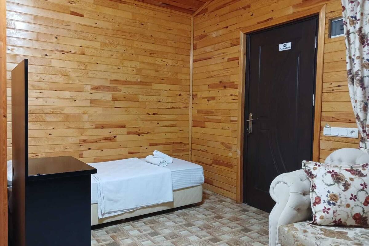 A small, wooden-paneled room with a bed, a sofa, and a door.