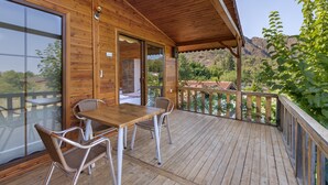 Terraza de madera con una mesa y sillas, con vistas a un paisaje montañoso.