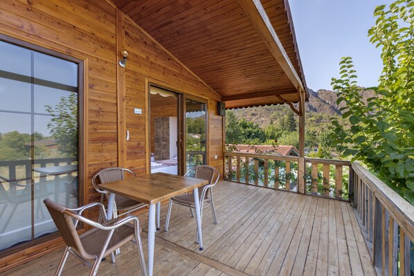 A wooden deck with a table and chairs, overlooking a mountainous landscape.