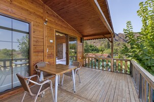 Terraza de madera con una mesa y sillas, con vistas a un paisaje montañoso.