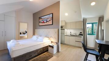 A bedroom with a bed, bedside table, and a mirror. Adjacent is a kitchenette with a microwave, sink, and cabinets. A dining area with a table and chairs is visible.