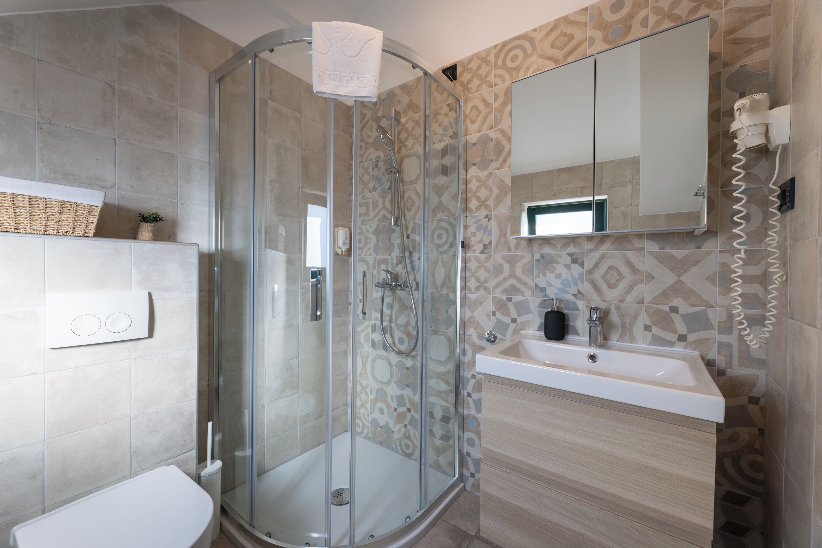 A modern bathroom with a glass-enclosed shower, a white sink, and a patterned tile backsplash.