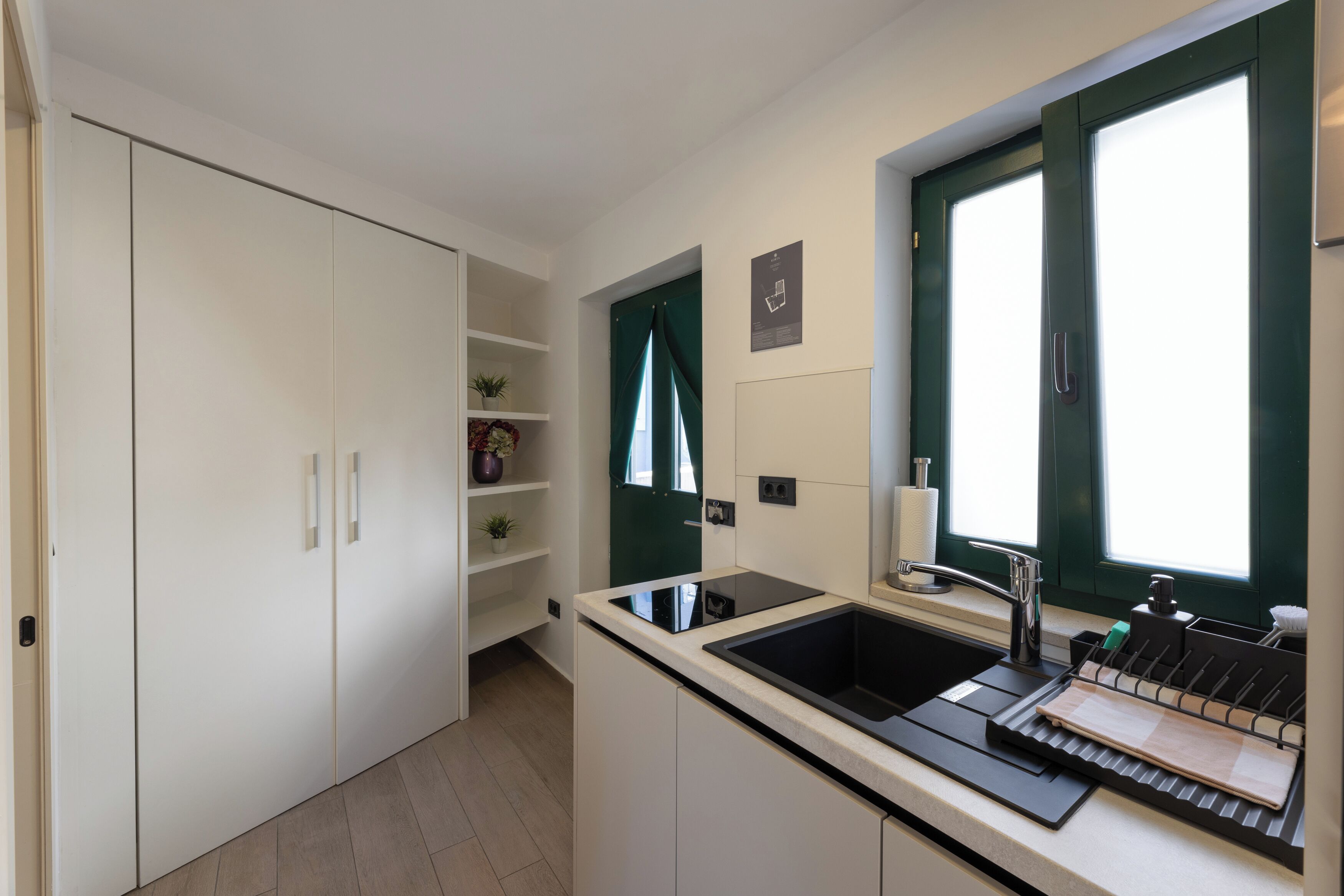 A compact kitchen with a black countertop, a sink, and a window with green curtains.