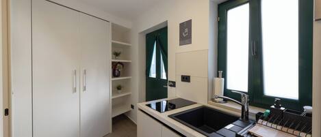 Cocina pequeña con cubierta negra, un lavamanos y una ventana con cortinas verdes.