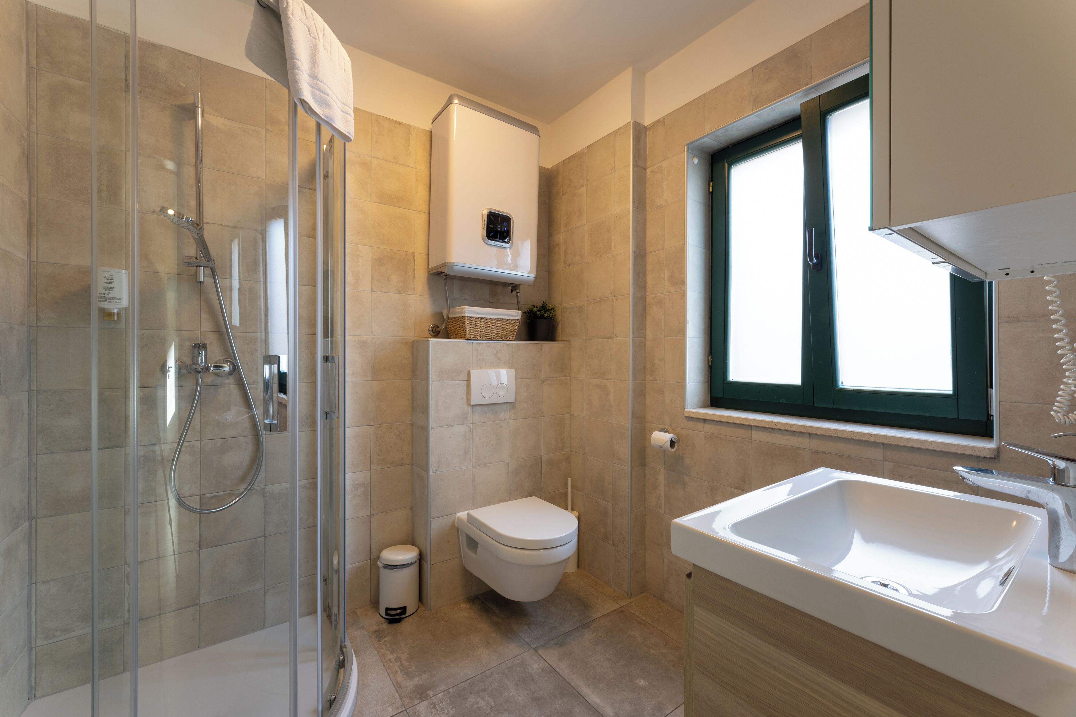 Un baño moderno con ducha envuelta en vidrio, inodoro blanco, lavamanos integrado y ventana que proporciona luz natural.
