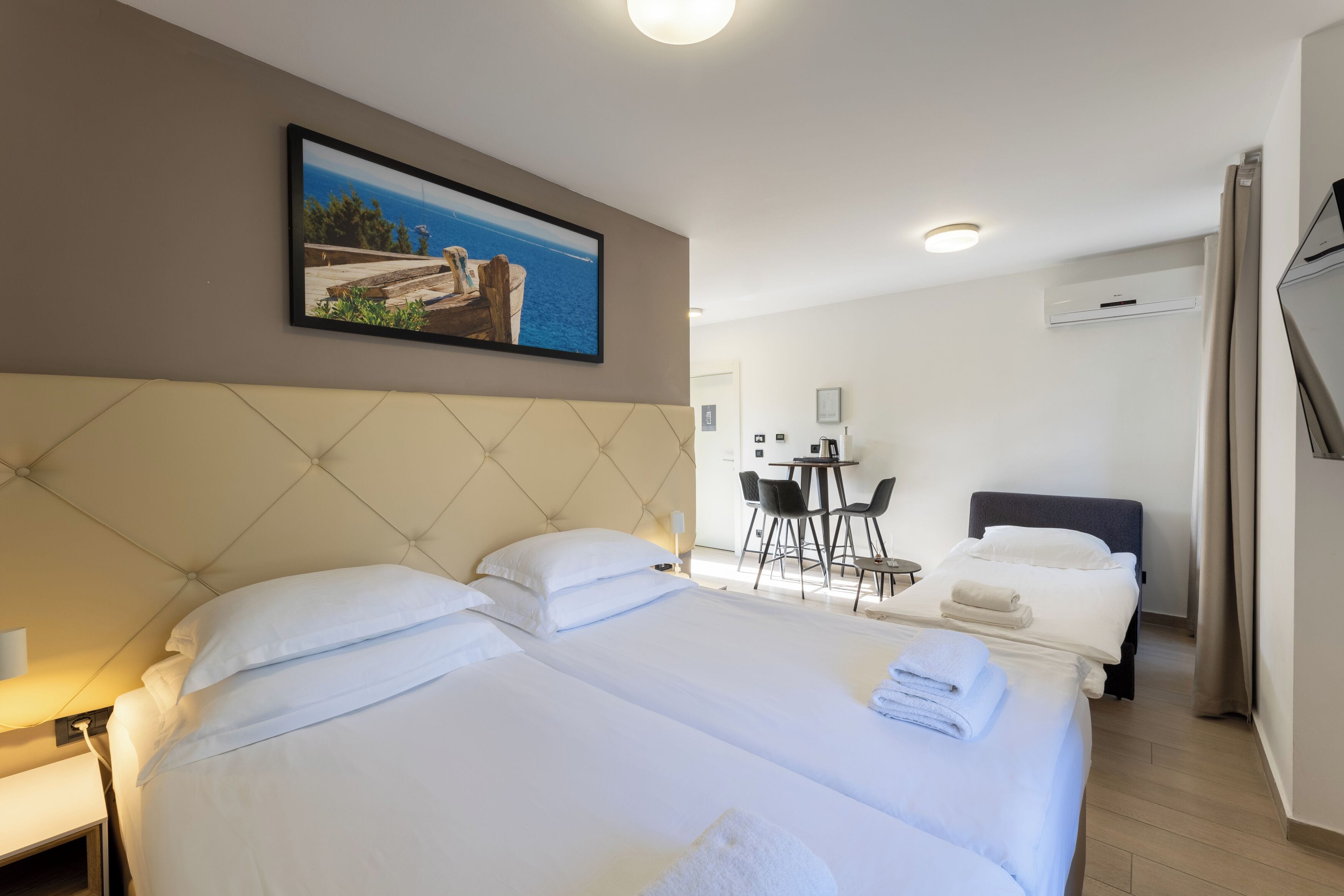 A hotel room with two beds, a dining area, and a view of the sea.
