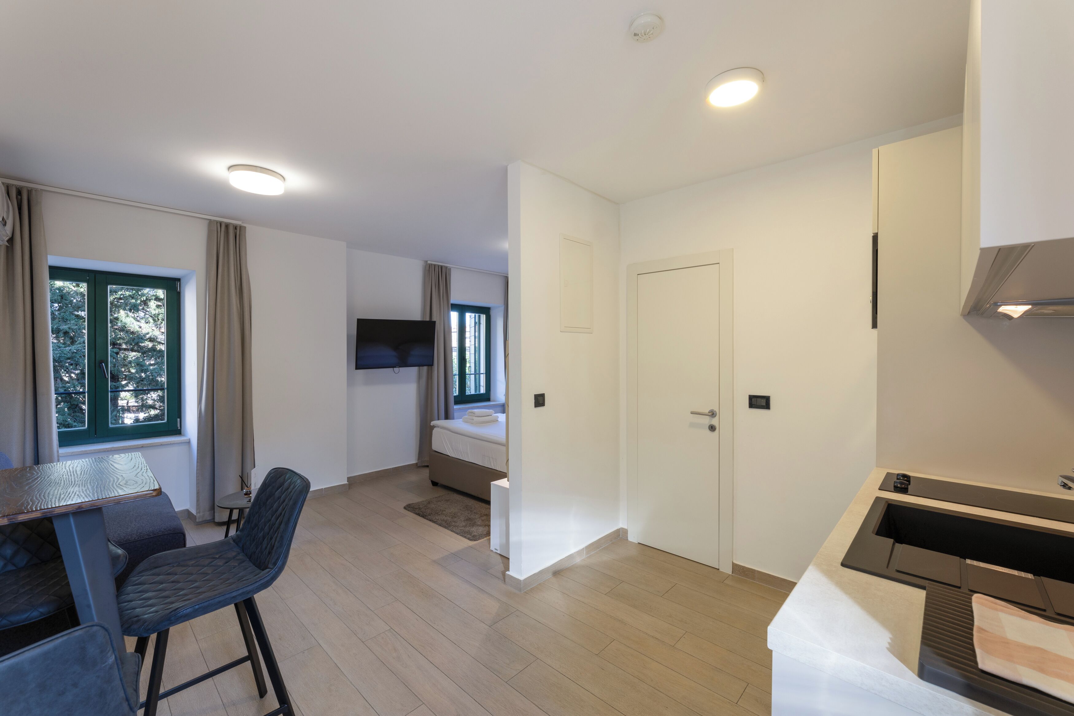 Ein modernes Hotelzimmer mit Essbereich, einem Bett, einem Fernseher und einer Küchenzeile.