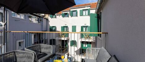 Ein Balkon mit Gartenmöbeln, einem Glastisch und einem großen Sonnenschirm.
