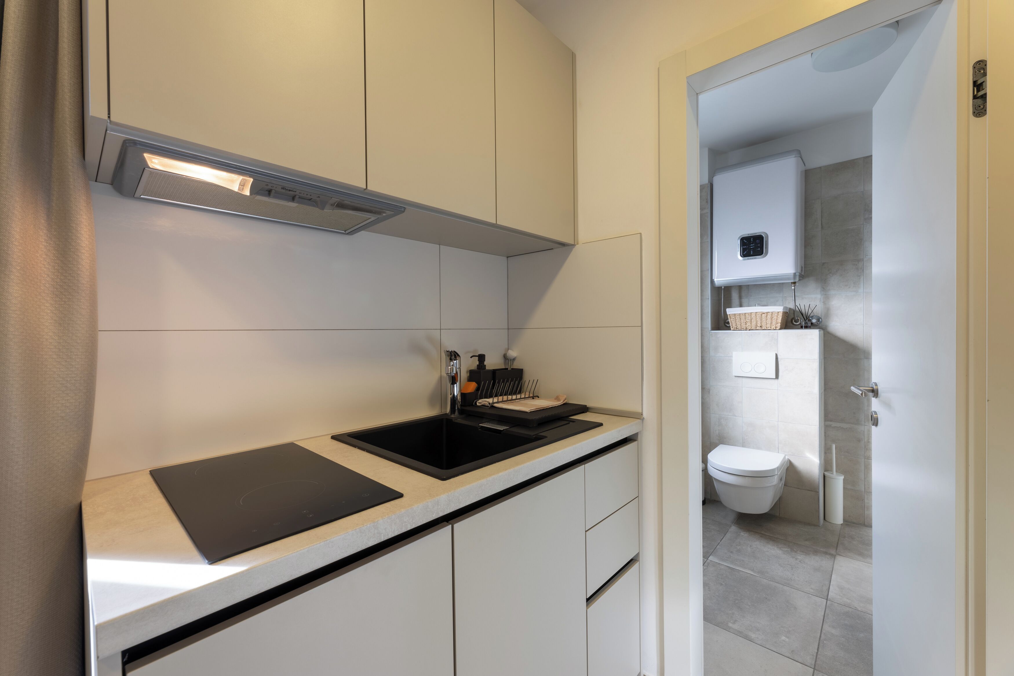 A modern kitchen with a black induction cooktop, a stainless steel range hood, and a white tiled backsplash.